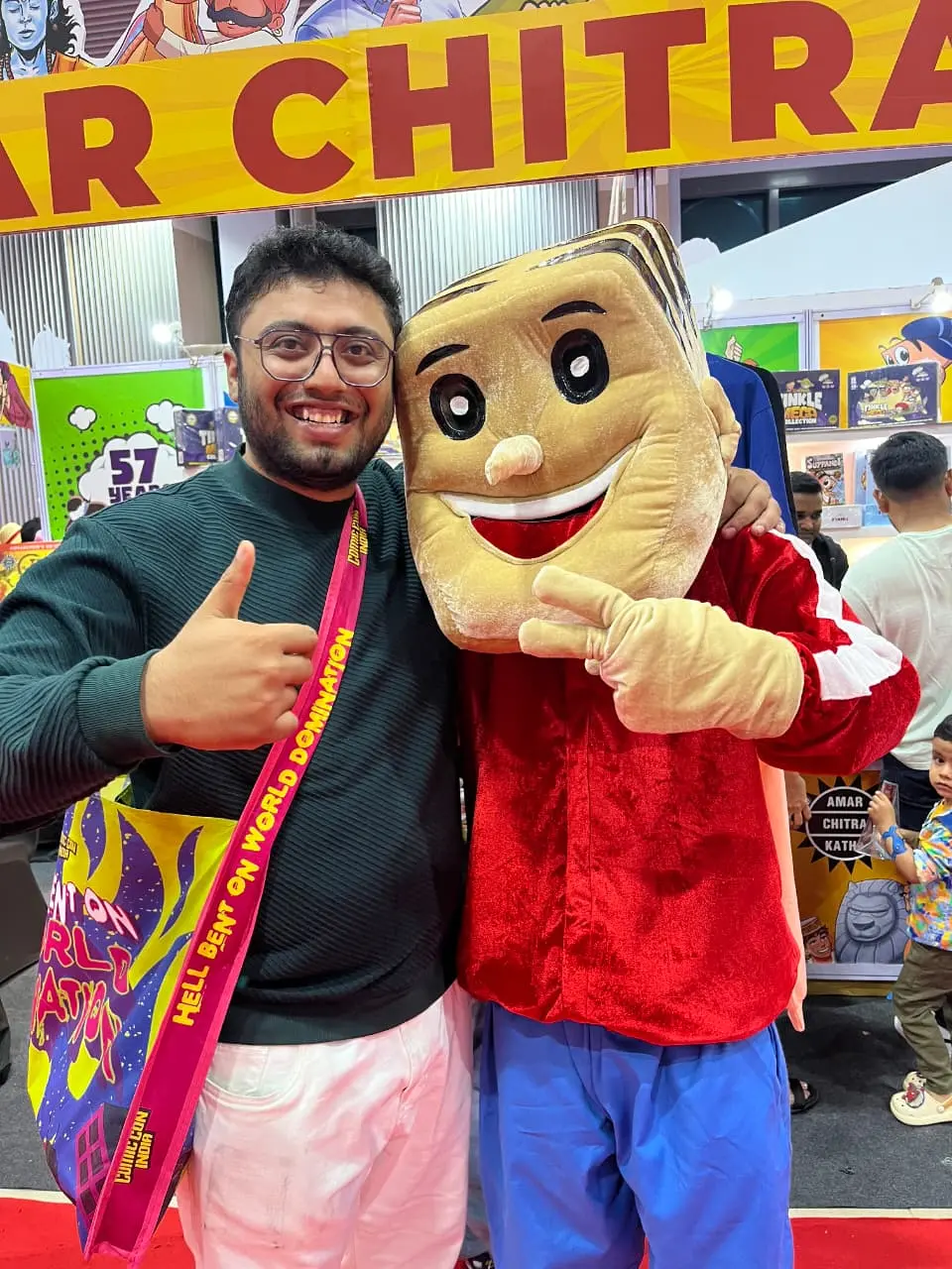 Raghavendra grinning next to the Suppandi mascot at an Amar Chitra Katha stall